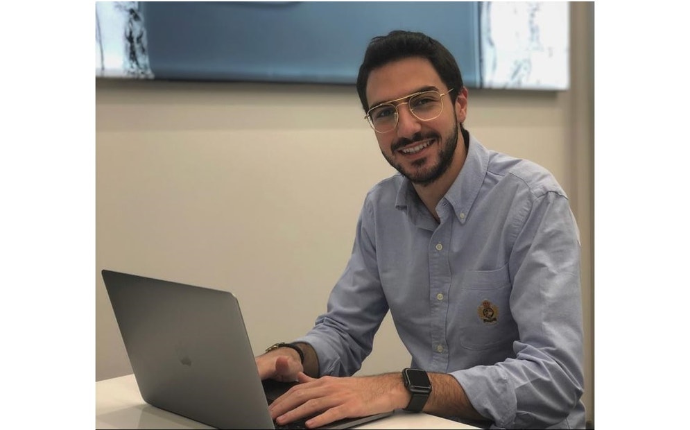 un homme est assis à un bureau et sourit à la caméra