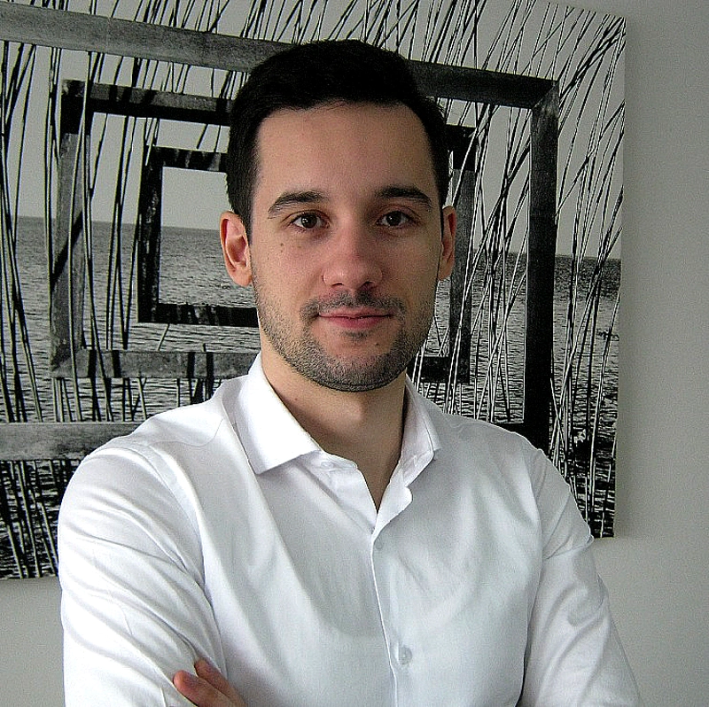 A man in a white shirt is seen in a portrait photo in front of a black and white photo on a wall