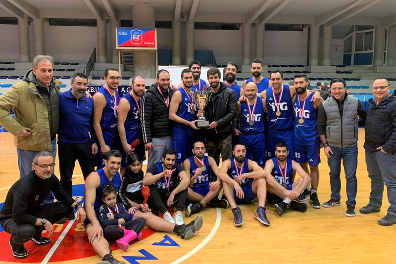 Group photograph of two teams holding a sports trophy