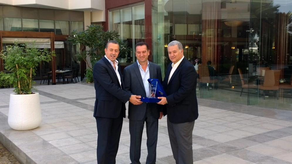 three men in suits hold a trophy