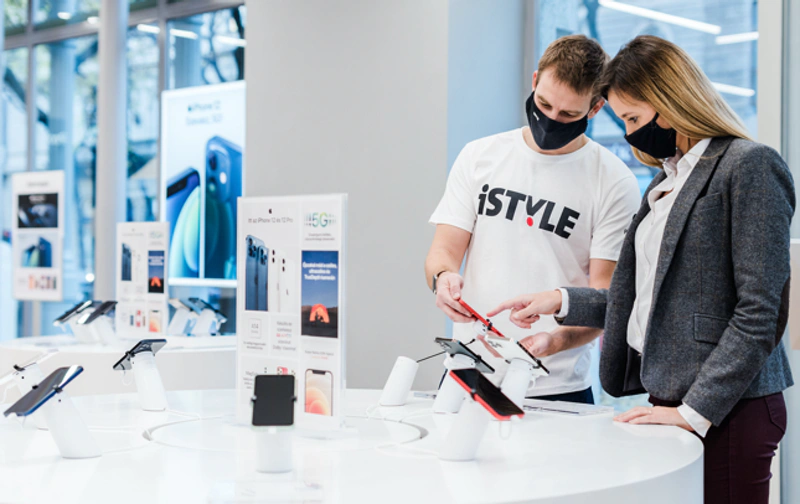 a man in a t shirt and a woman in a business suit stand are discussing iphones in a hi tech retail site