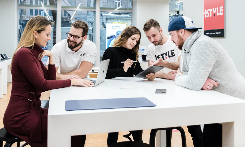 five people are seen looking at Apple laptops in a hi tech store