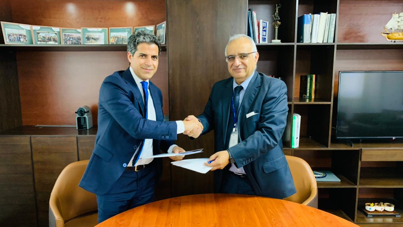 two men exchange agreements across a table and shake hands