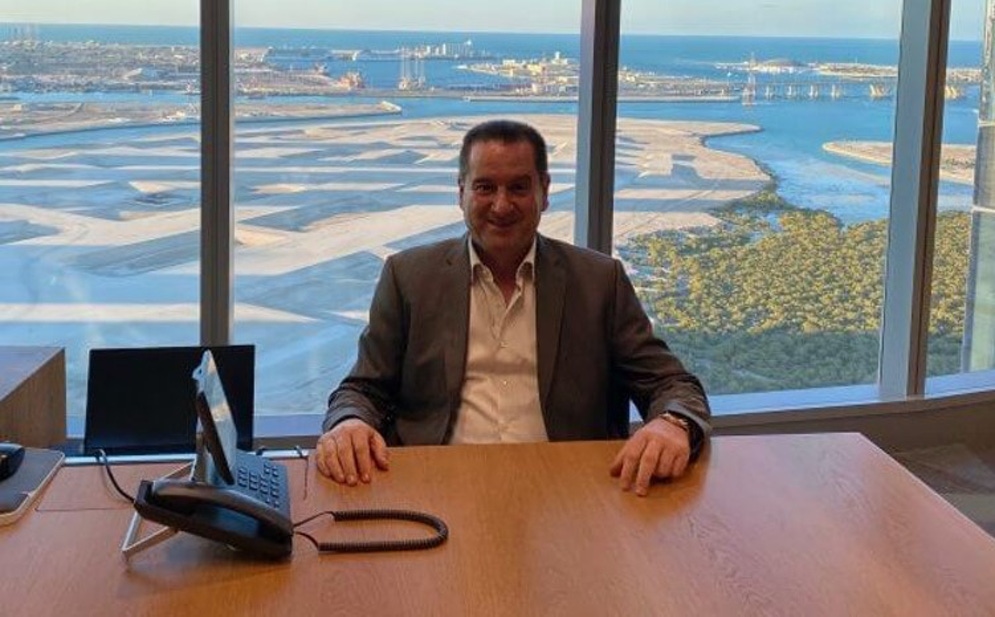 a man in a suit sits at a desk in front of a panoramic window