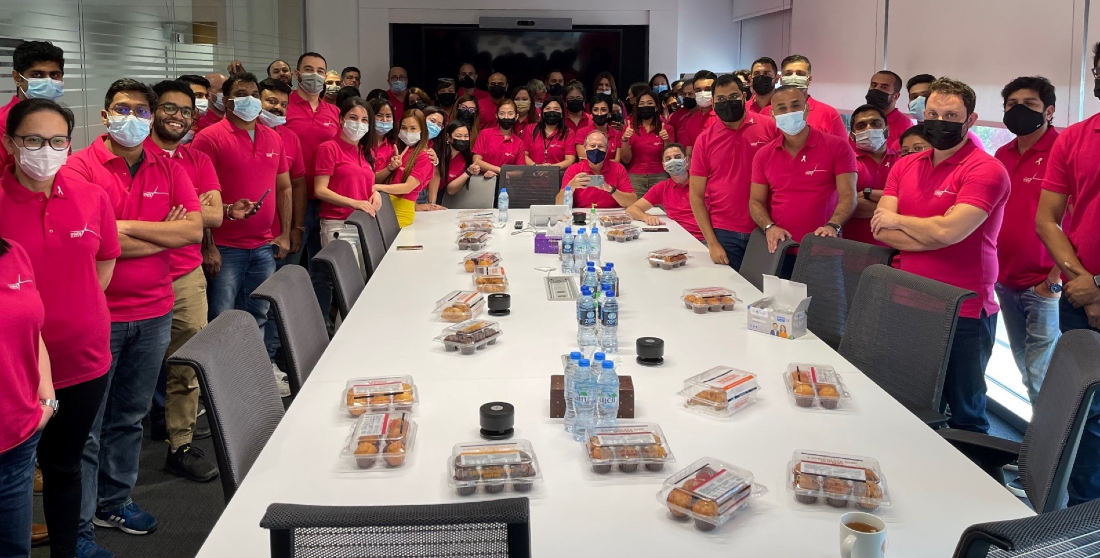 shows a group of people gathered around a large table each wearing a pink t-shirt