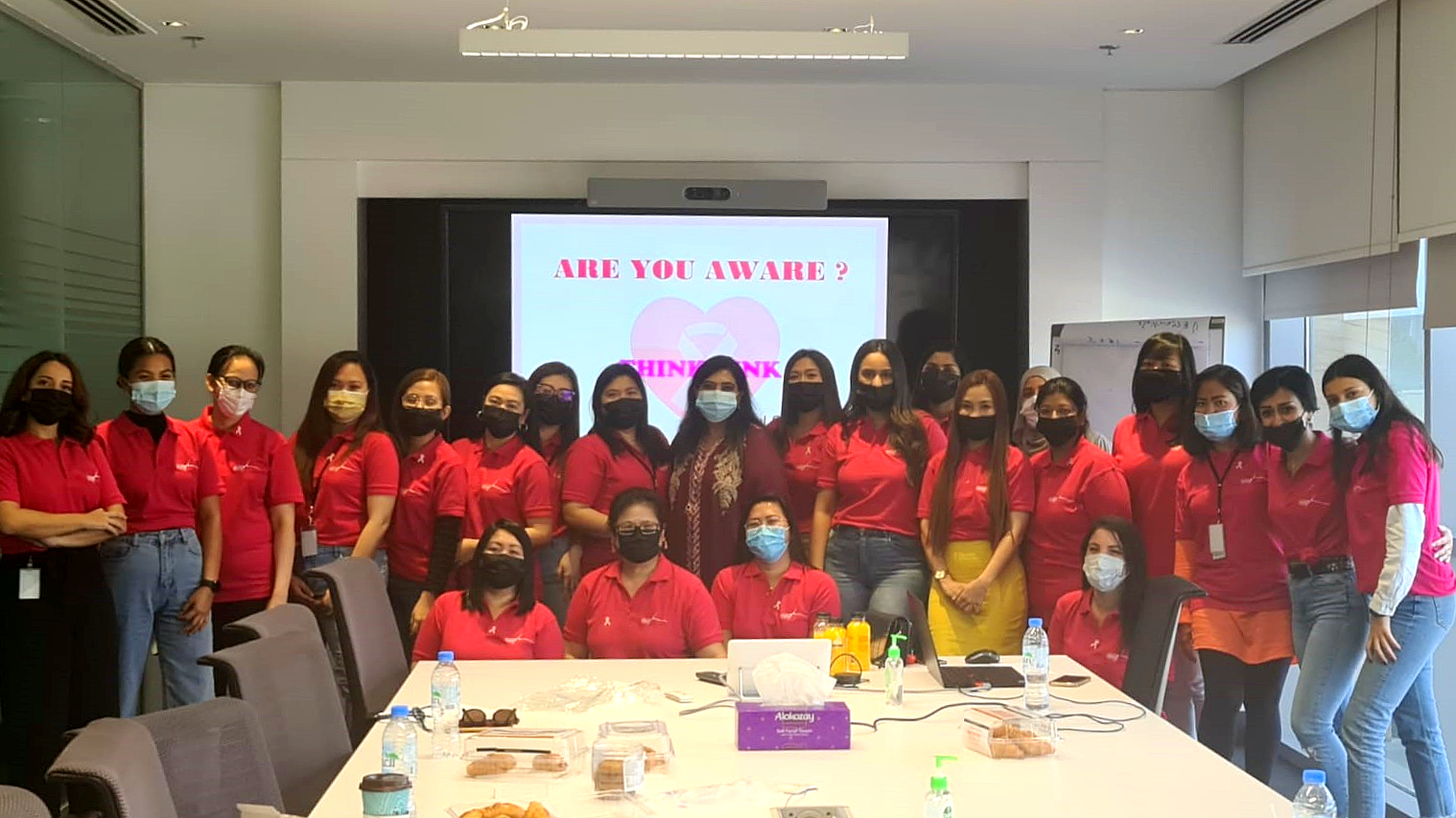 a group photo of people gathered around a table all wearing red and pink t-shirts