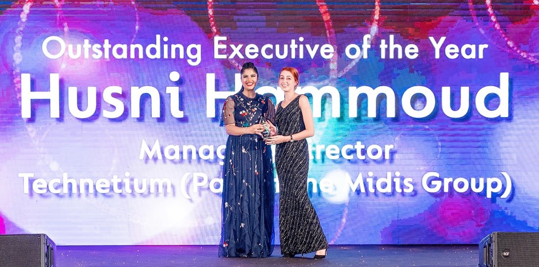 two women are on a presentation stage as a trophy is awarded