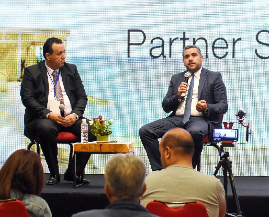 Two men are seen on stage in a discussion