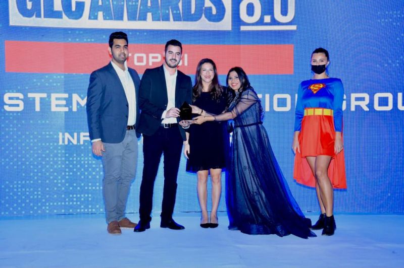 five people on an event stage are seen as an award is handed over