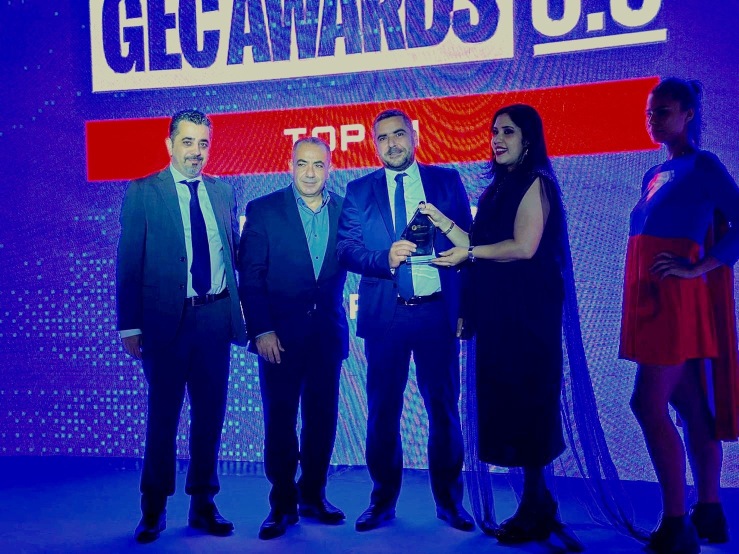 three men accept an award from a women on stage