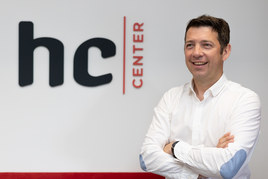 a man is seen with folded arms in front of a company logo spelling HC Center