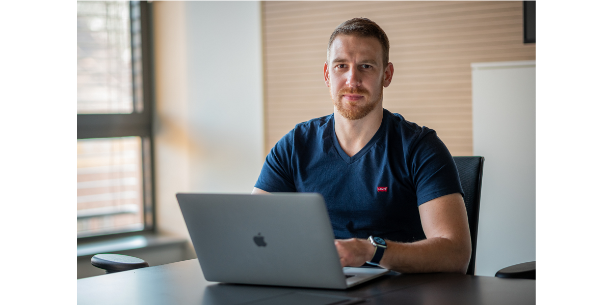 a man sitting at a desk with an Apple laptop