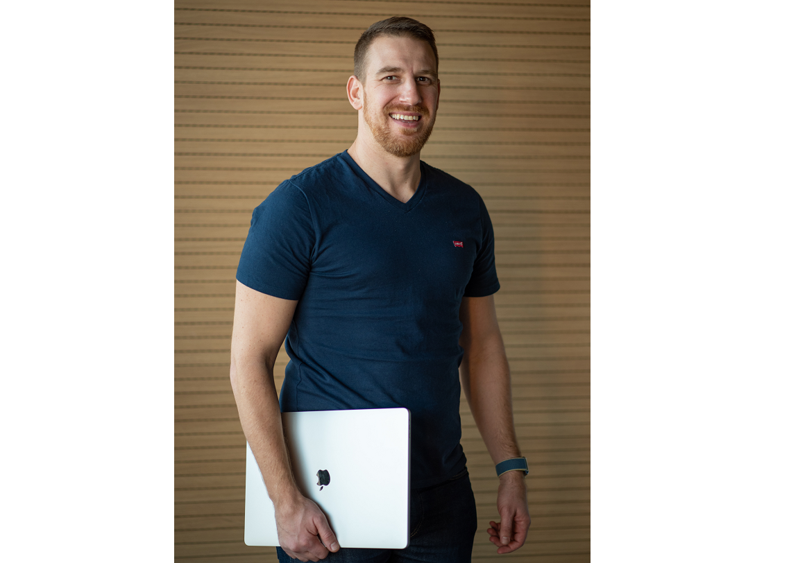 a man is seen in a head and shoulders view holding an Apple laptop 