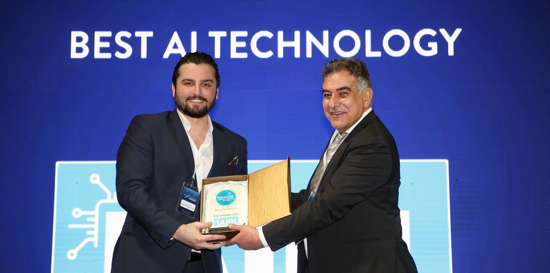 two men are seen against a backdrop, one man passing an award to the other