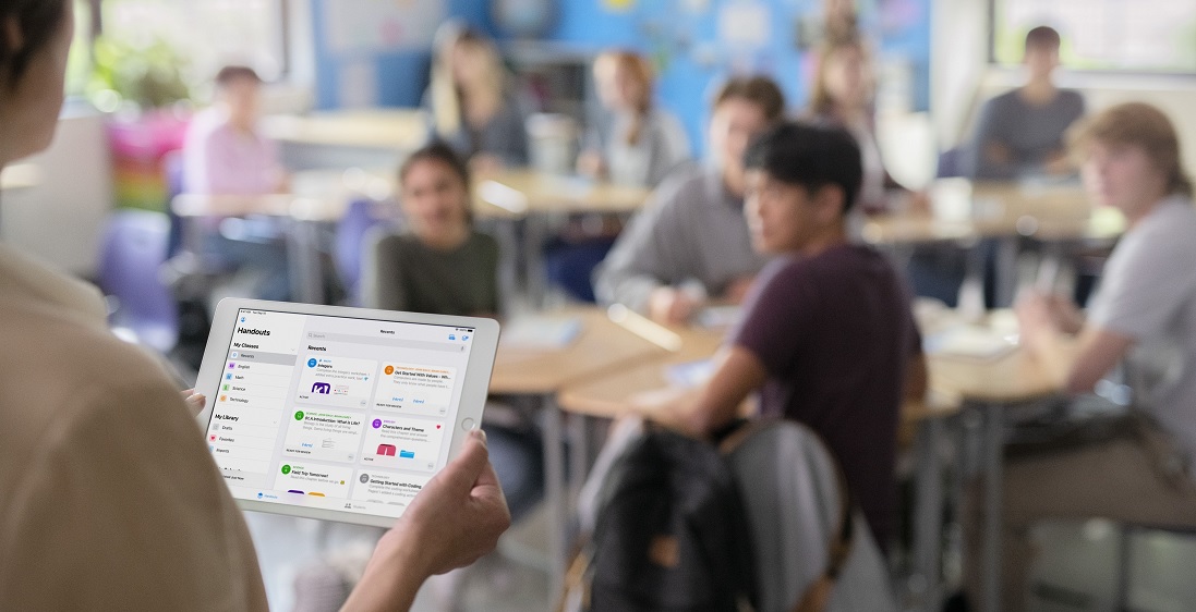 a teacher holds a tablet computer in front of a class of students