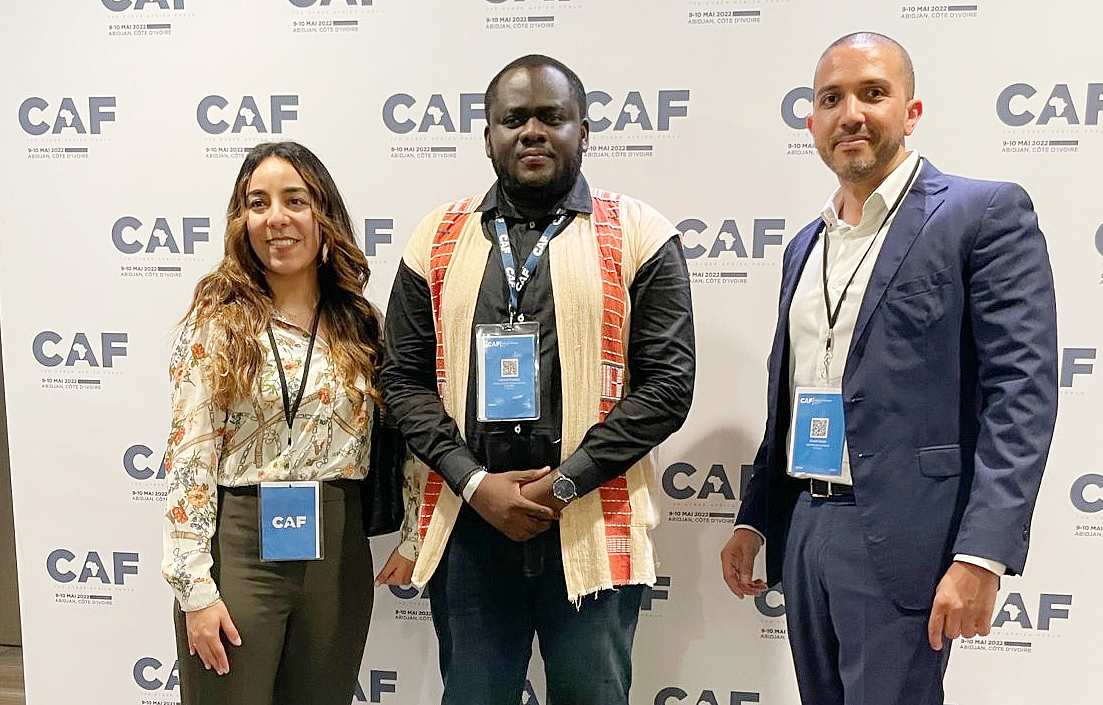 Three people stand together at an event with the words CAF seen on a background