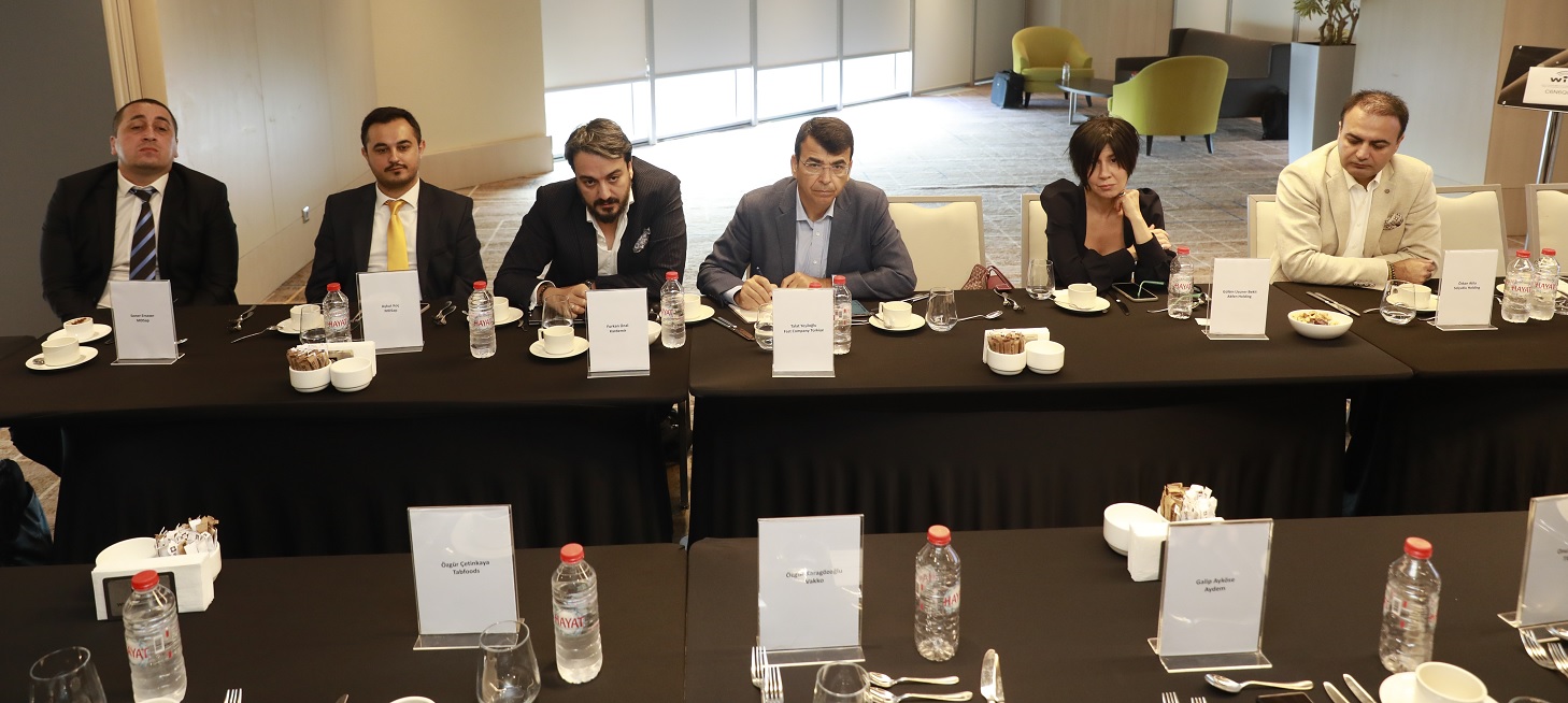 six people are seated at a board table and are listening to a speaker