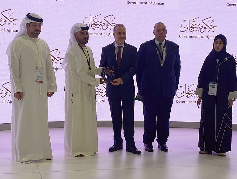 5 people are seen on a presentation stage as one hands over a trophy