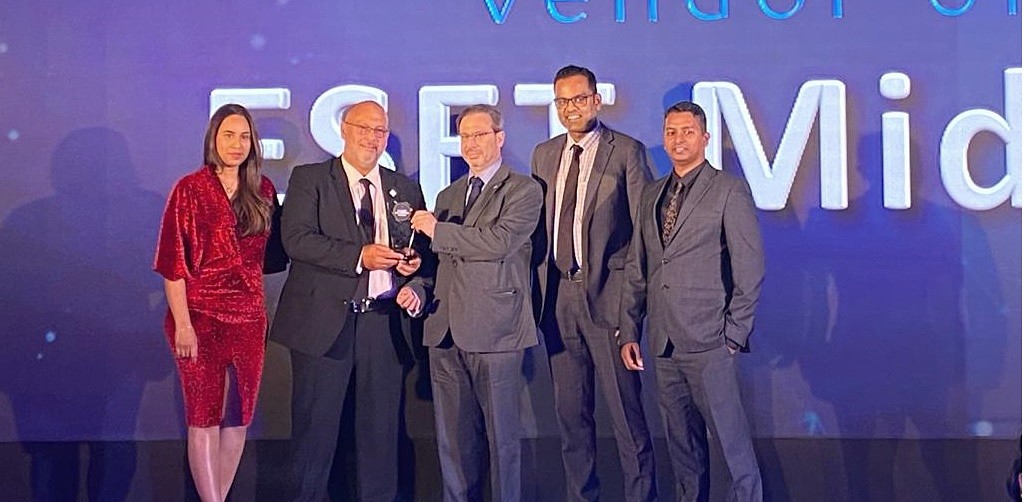 five people are seen on a presentation stage as a trophy is handed over