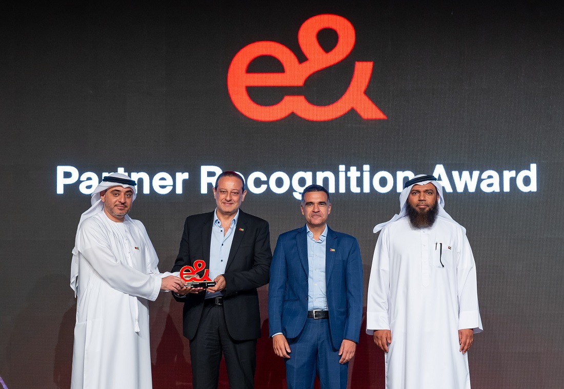 four men are seen together on a presentation stage as an award trophy is handed over