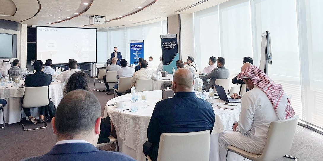 a room full of people with a presenter speaking in front of a screen