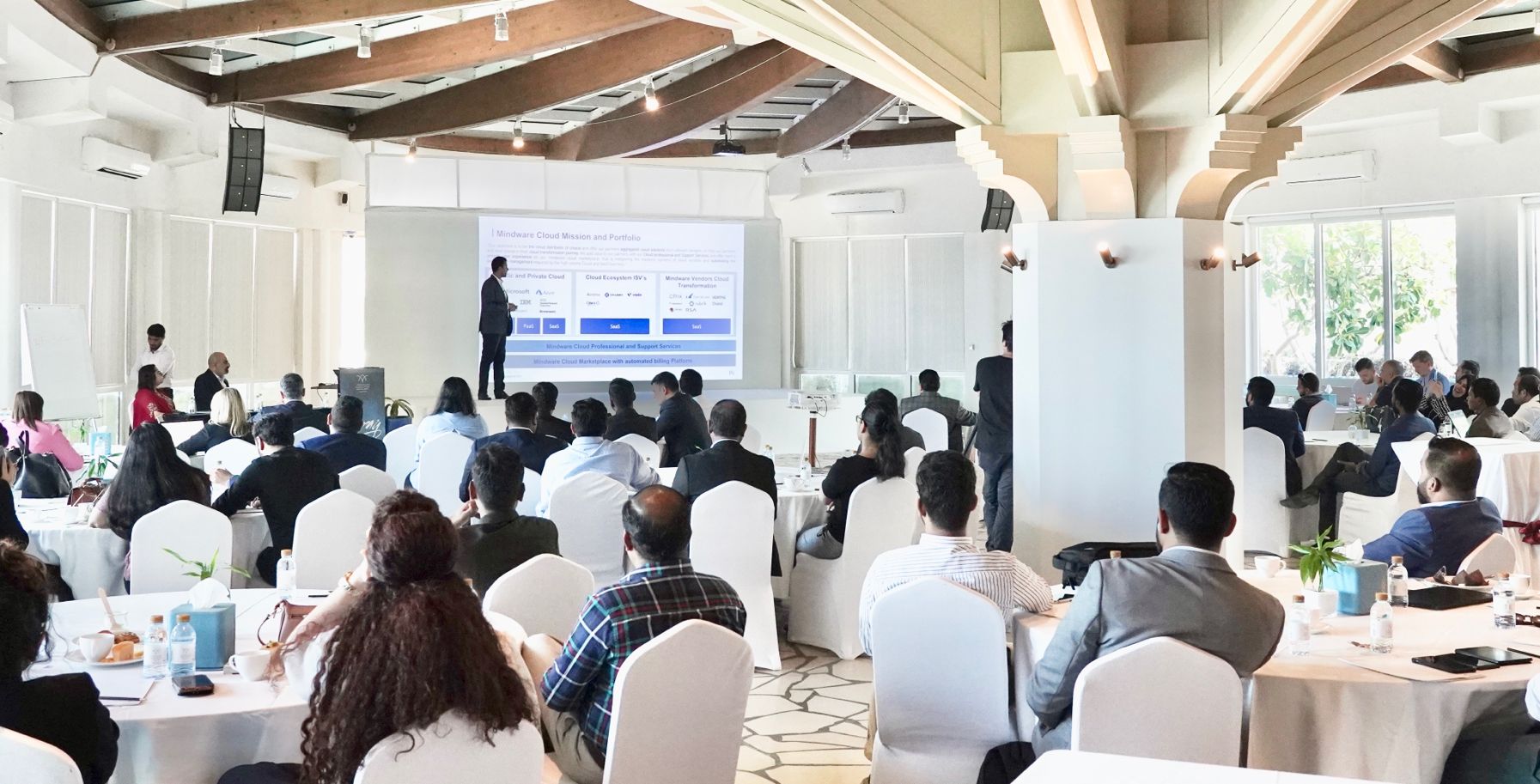 large group of people in the foreground watch a man making a presentation