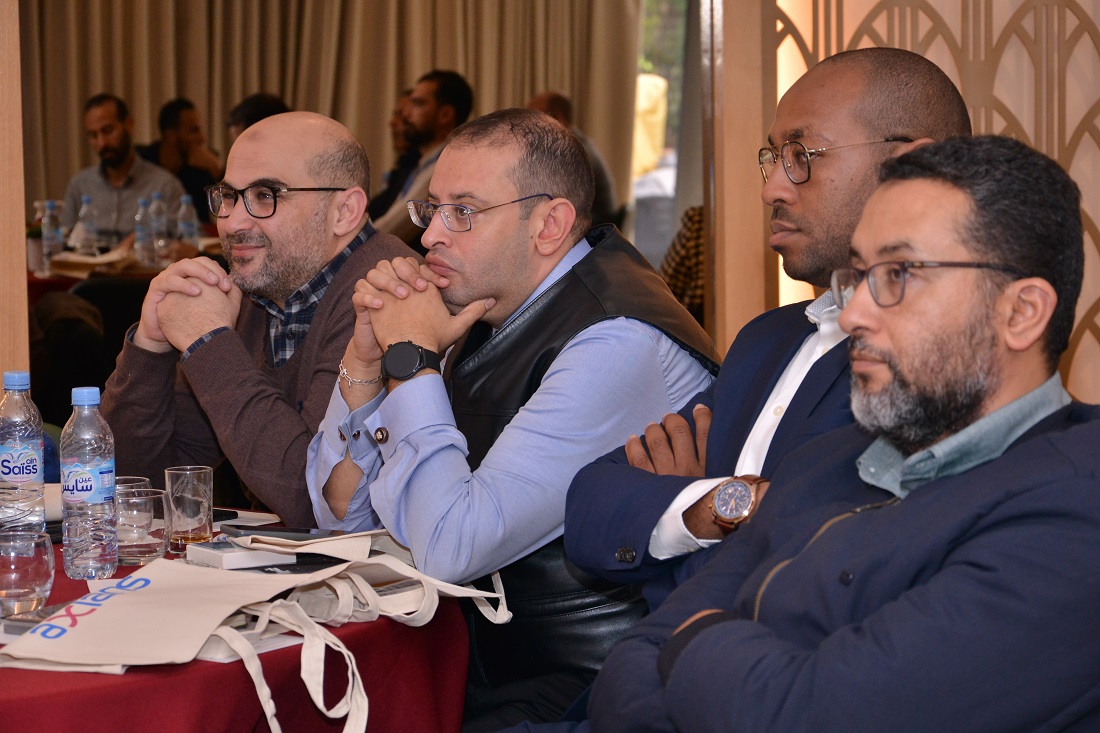 four men are seen at a table watching a presentation