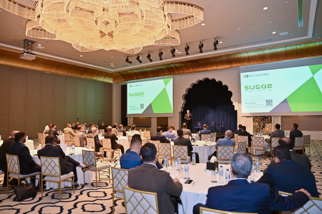 a room full of executives is seen with a figure at the head of the room leading the discussion