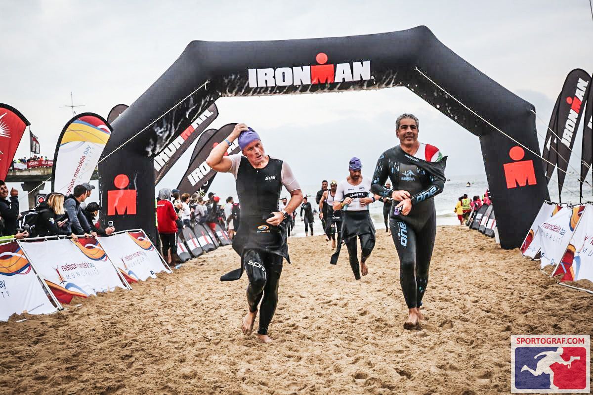 two men are seen running under an archway, removing wetsuits