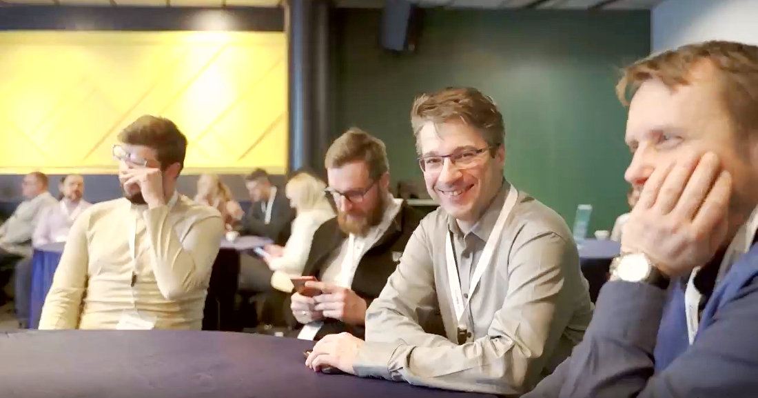 a group of men are sitting a table watching a presentation