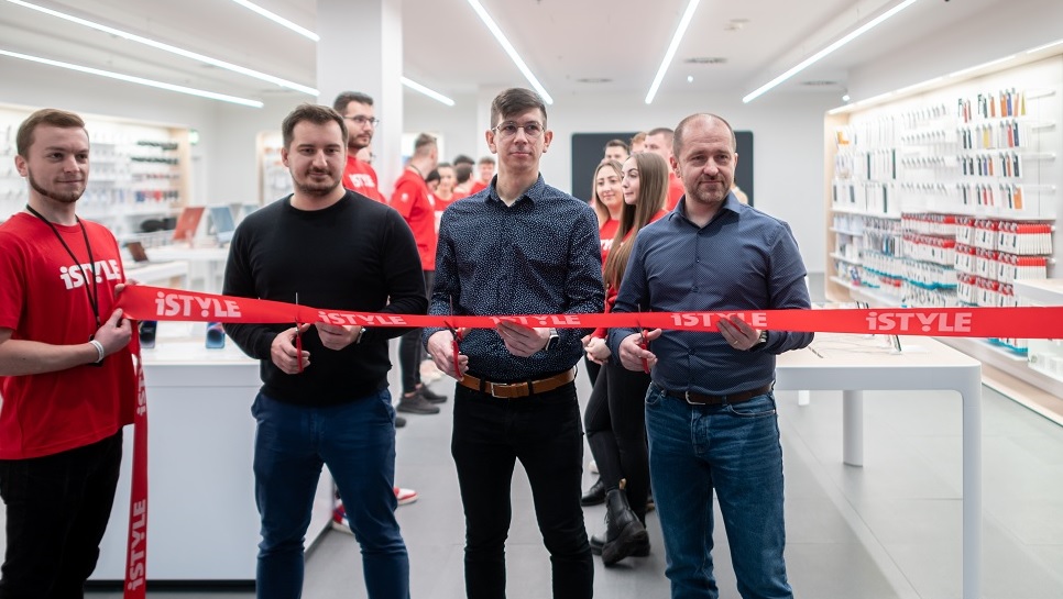 four men stand in the doorway of a hi tech store just about to cut a red ribbon