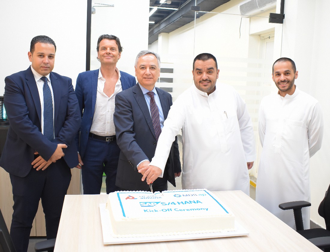 five men are seen around a table where a cake is being cut