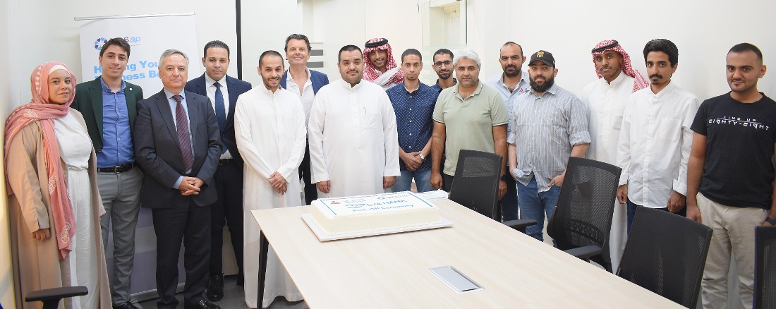 group photo of people standing near a table with a decorated cake in the foreground