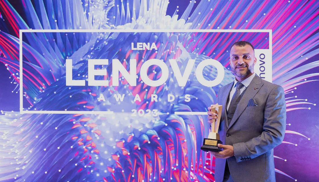 a man holds a trophy at a presentation in front of a screen with the word Lenovo prominently displayed