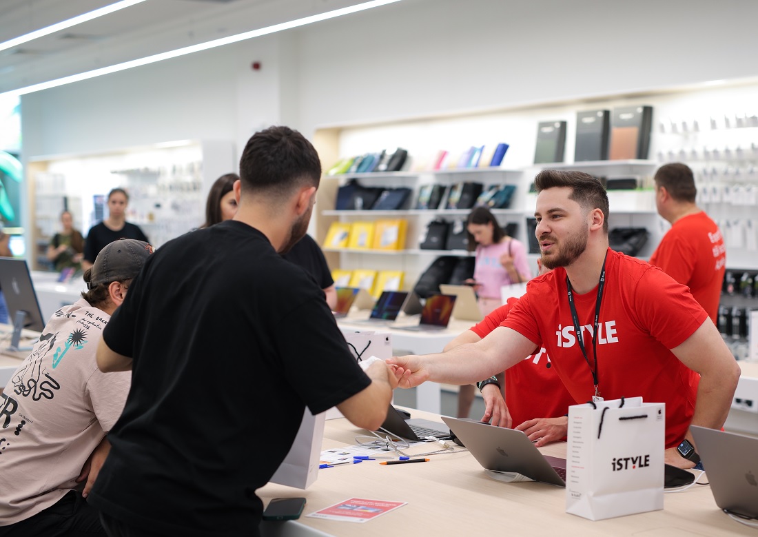 a man in a red t-shirt with the word iSTYLE is seen handing goods to a customer in a black t-shirt