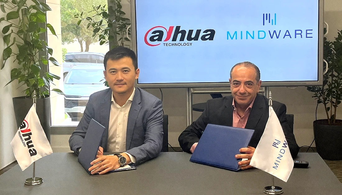 two men are side by side at a table as they sign an agreement