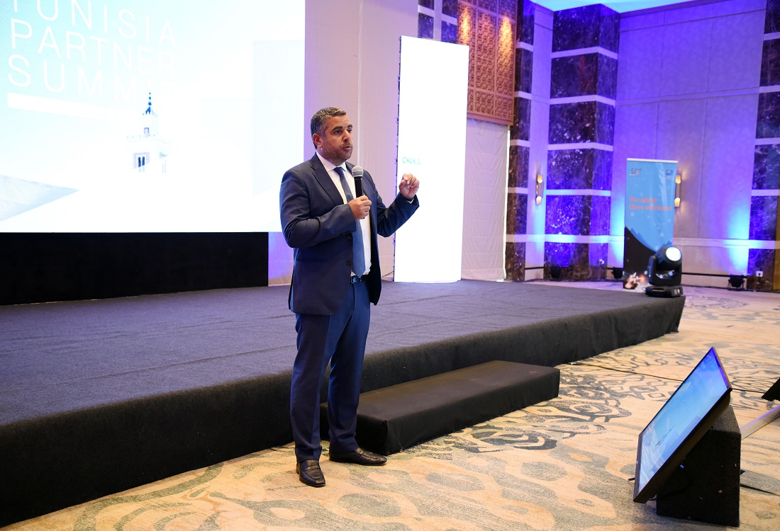 a man in a suit and tie is presenting to an audience in front of a digital screen