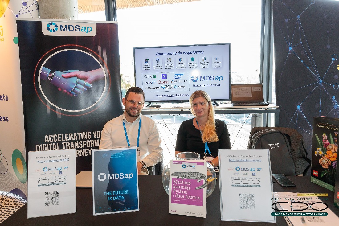 two people - a man and a woman - sit at an exhibition stand at an IT conference