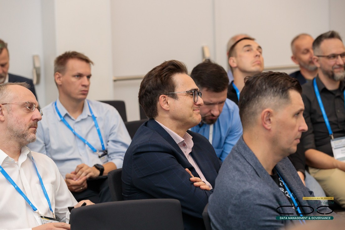 eight men, sitting at tables, are seen watching a presentation