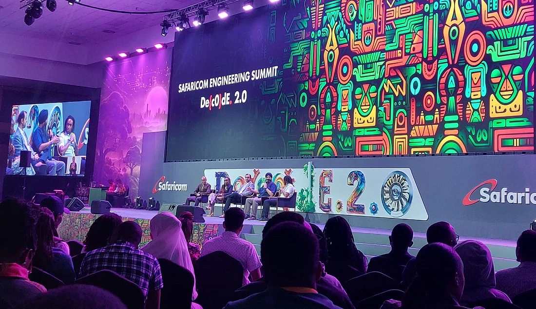people are seen on a presentation stage with a colourful backdrop spelling out the word Decode 2.0