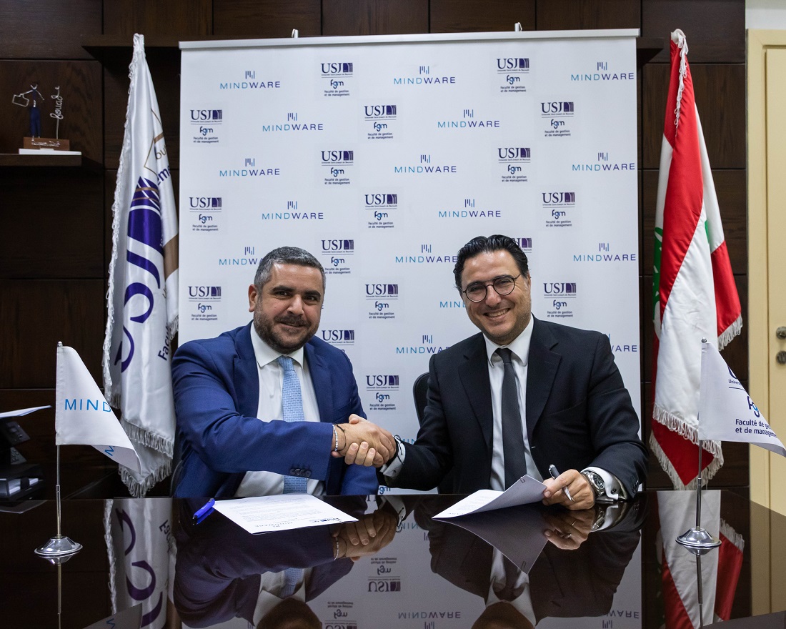 Two men are seen sitting at a desk signing an agreement