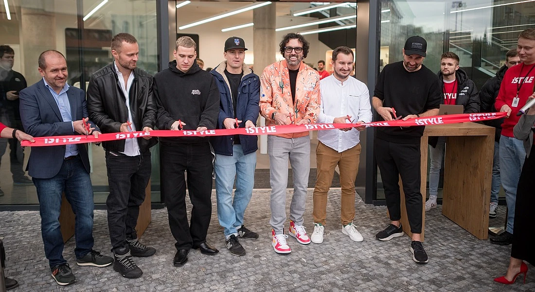 shows a group of people holding a red ribbon and getting ready to cut it to open a retail site
