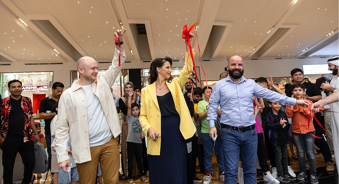 three people are seen holding ribbons cut to open a shop