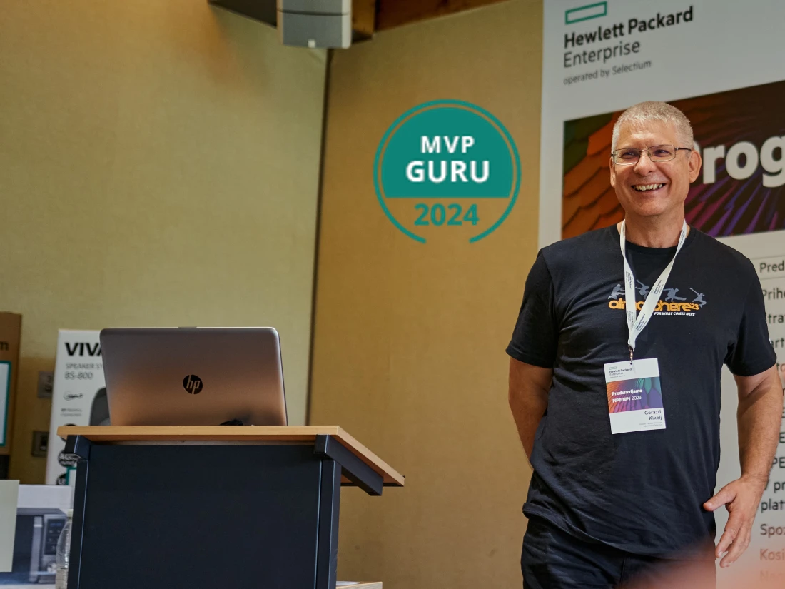 a man in a black t shirt is seen next to a presentation stand with a laptop on it