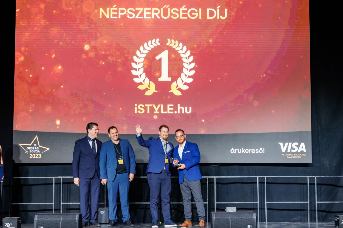 four men are seen on a presentation stage with two on the right holding a trophy