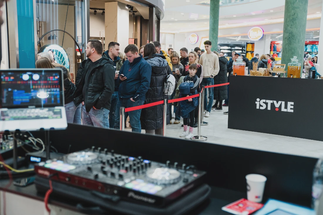 a queue of people are seen in the background with a dj desk in the foreground