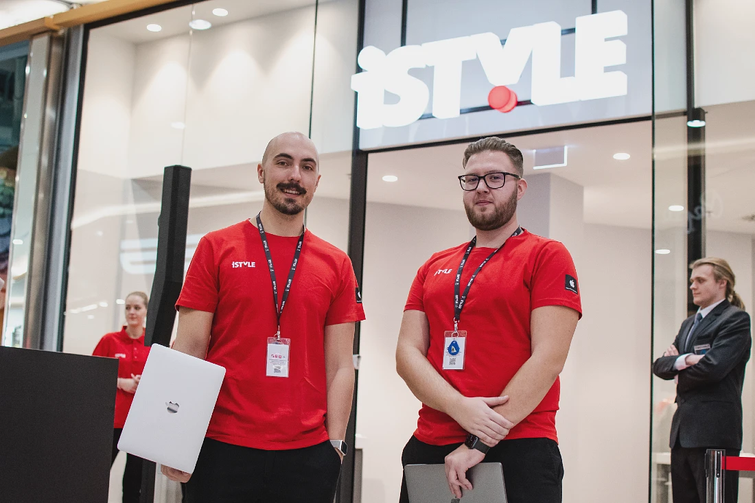 deux hommes portent des t-shirts rouges avec une grande enseigne de magasin au-dessus d'eux en arrière-plan, exhibant le mot iSTYLE