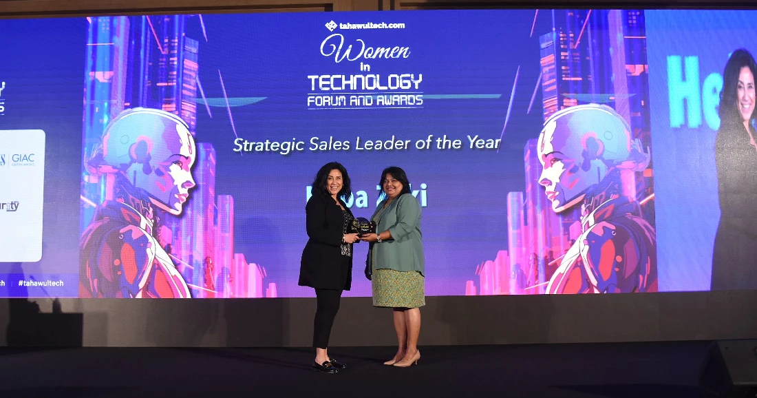 two women are seen on a presentation stage as an award trophy is handed over