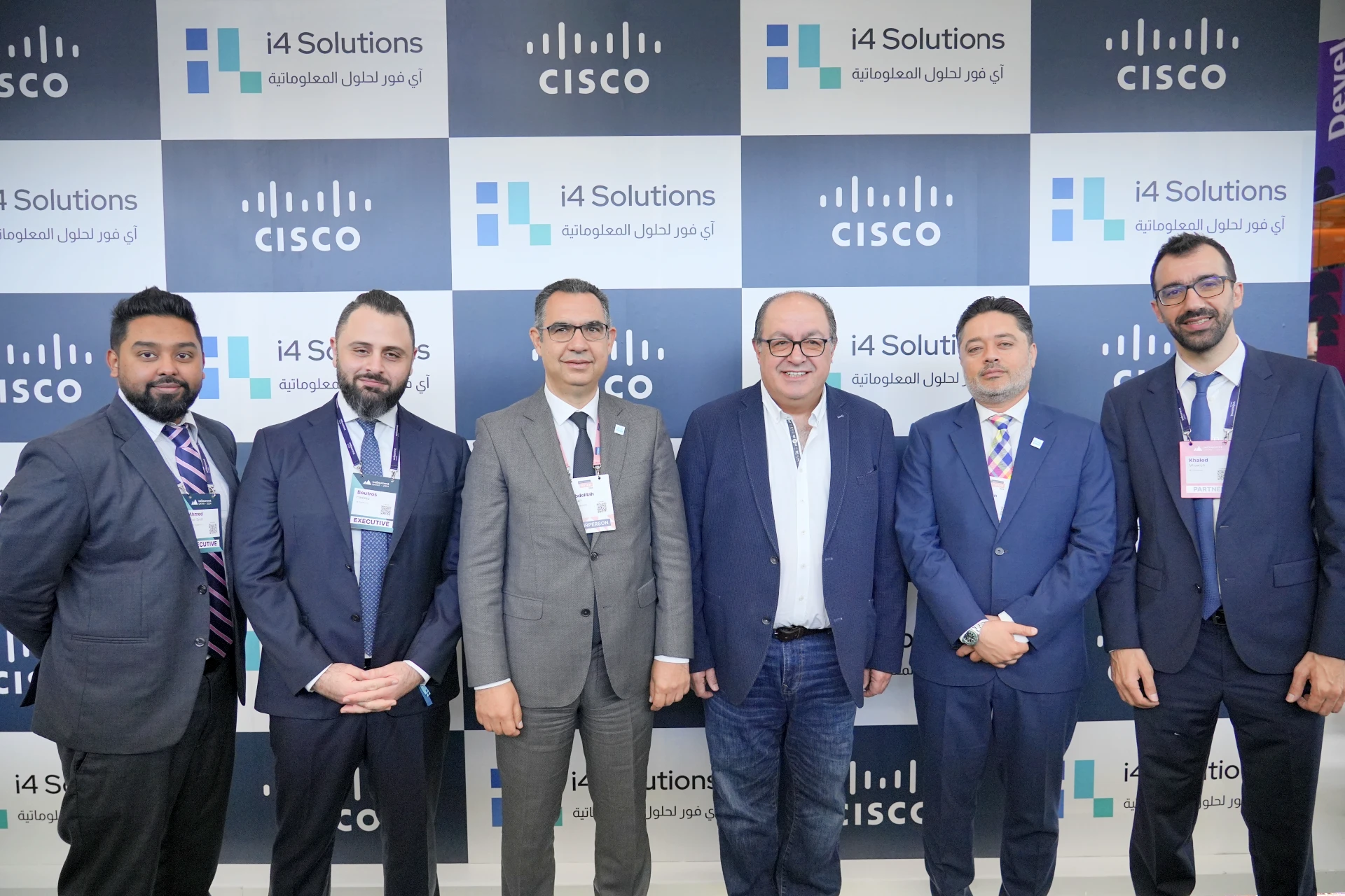 six hommes en costume sont vus devant un présentoir avec les logos i4 et Cisco bien visibles.