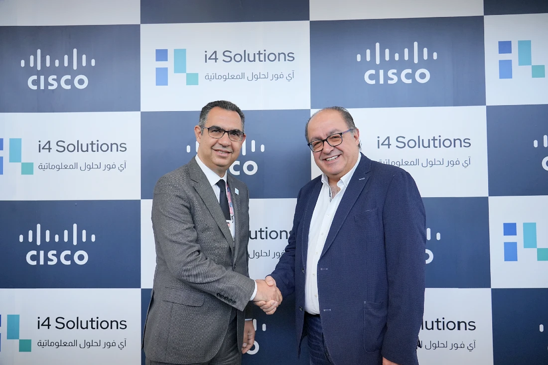 Two men shake hands in front of a display background, with the i4 and Cisco logos prominently seen